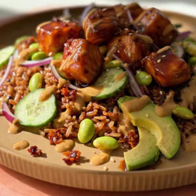 A bowl of salmon, rice, avocado and vegetables on a light worktop
