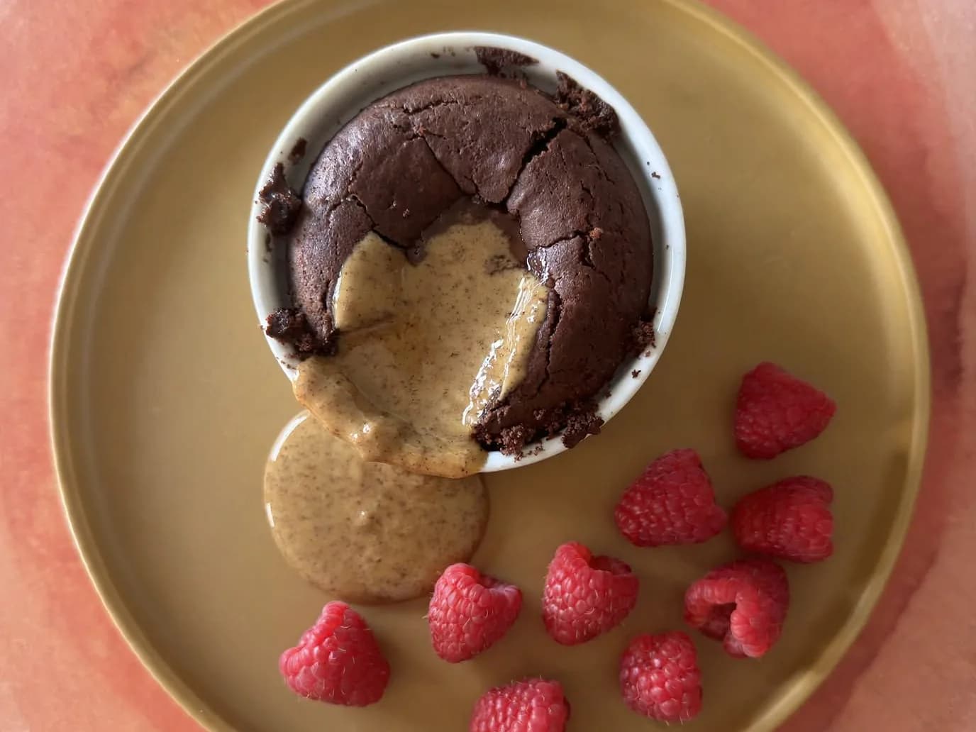 Chocolate cake in a ramekin with a runny almond butter centre, fresh raspberries on the side