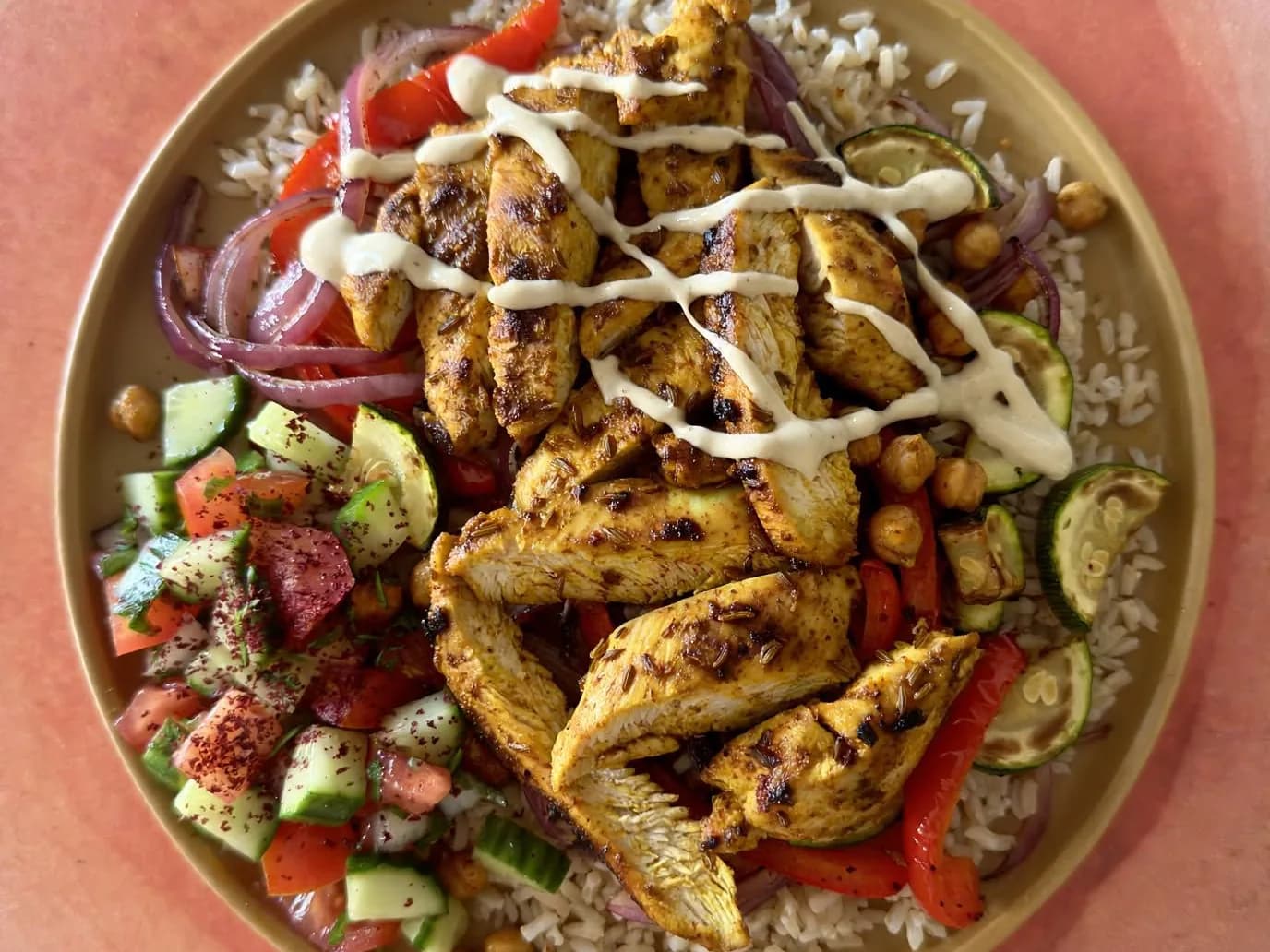 Strips of chicken shawarma on rice with roasted pepper, courgette, chickpeas and salad, drizzled with tahini sauce